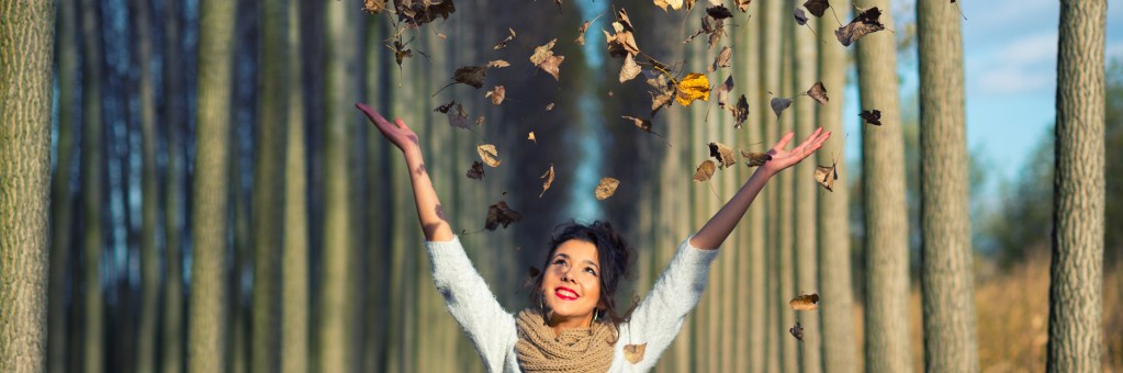 Smiling woman in white throwing leaves in an arc over her head.
