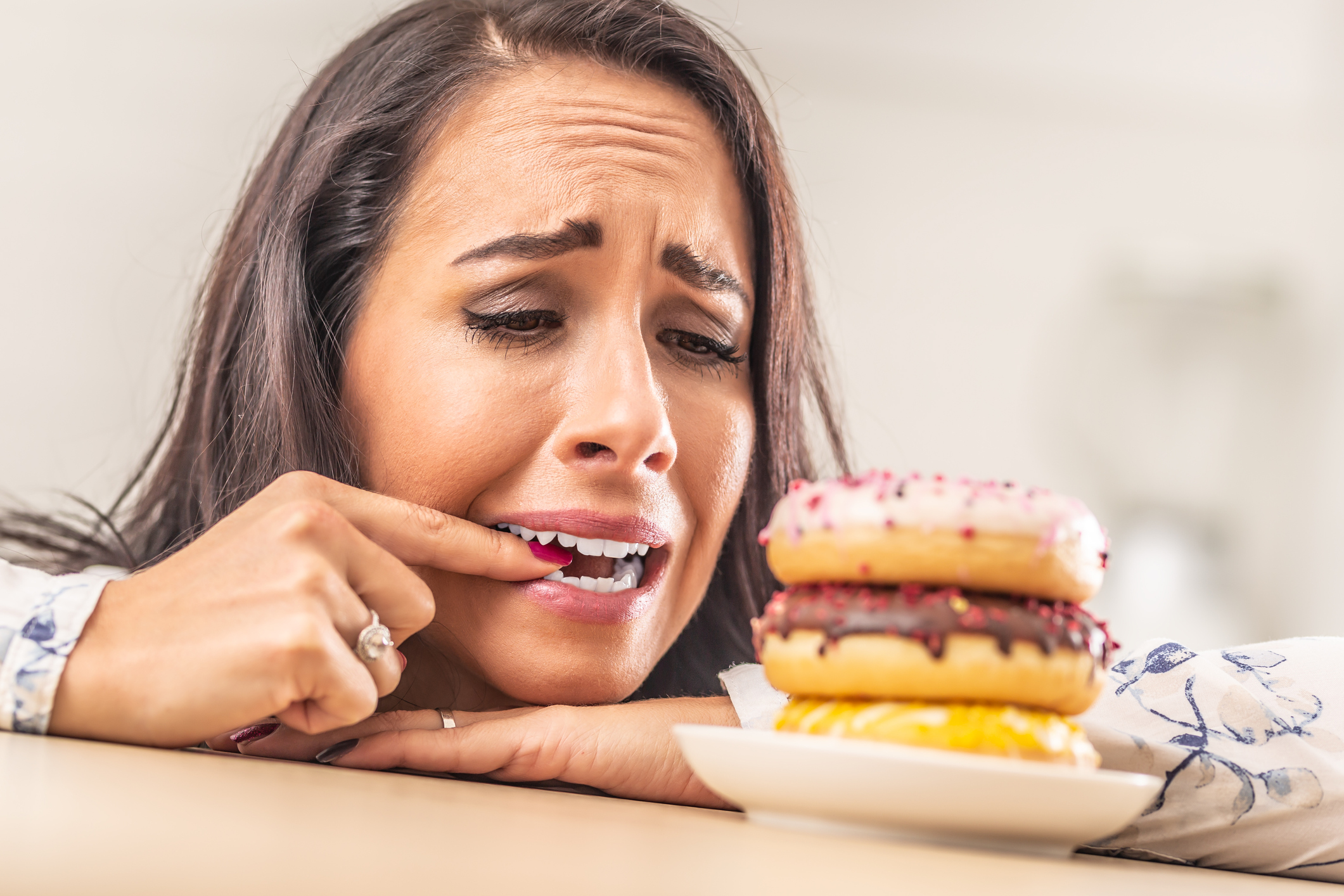 Woman biting the nail of her forefinger to prevent her hand from taking a donut.
